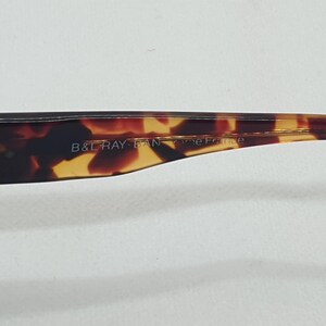 Puede incluir: Primer plano de la patilla de unas gafas con estampado de carey. El texto "B & RAY BAN" es visible en la patilla. Las gafas tienen una bisagra plateada y un dise&ntilde;o curvado.