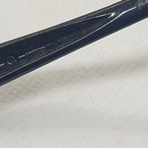 Puede incluir: Primer plano de un objeto negro y delgado con un extremo puntiagudo y una peque&ntilde;a abertura ovalada. El objeto tiene un acabado brillante y parece estar hecho de un material duro. El fondo es una superficie lisa de color blanquecino.