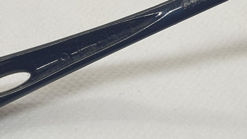 Puede incluir: Primer plano de un objeto negro y delgado con un extremo puntiagudo y una peque&ntilde;a abertura ovalada. El objeto tiene un acabado brillante y parece estar hecho de un material duro. El fondo es una superficie lisa de color blanquecino.