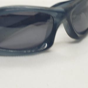 May include: Dark blue sunglasses with a curved frame and dark lenses. The sunglasses have a sporty design and are suitable for outdoor activities. The frame appears to be made of a durable plastic material.