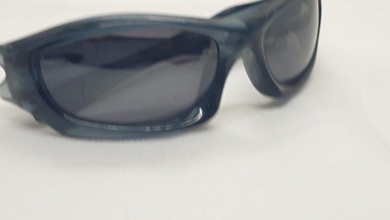 May include: Dark blue sunglasses with a curved frame and dark lenses. The sunglasses have a sporty design and are suitable for outdoor activities. The frame appears to be made of a durable plastic material.