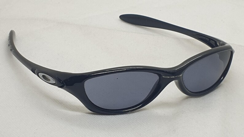 Puede incluir: Gafas de sol negras con un dise&ntilde;o elegante y curvado. Las lentes son de color gris oscuro y las monturas negras brillantes. Las patillas presentan un peque&ntilde;o logotipo plateado. Estas gafas ofrecen una est&eacute;tica moderna y deportiva.