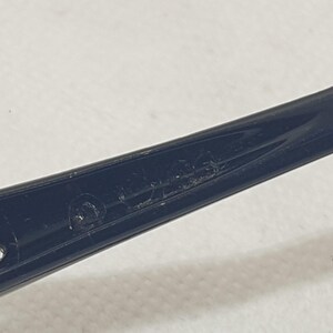 Puede incluir: Primer plano de una patilla de montura de gafas negra. La patilla tiene un dise&ntilde;o curvado con un peque&ntilde;o agujero cerca de la parte delantera. El texto "MADE" es visible en la patilla.