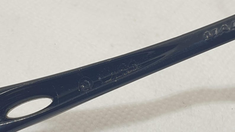 Puede incluir: Primer plano de una patilla de montura de gafas negra. La patilla tiene un dise&ntilde;o curvado con un peque&ntilde;o agujero cerca de la parte delantera. El texto "MADE" es visible en la patilla.