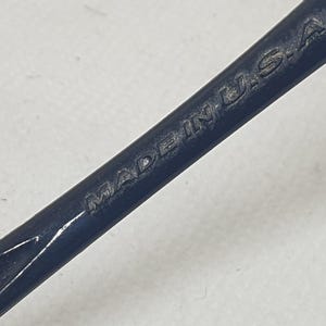 Puede incluir: Primer plano de una herramienta de metal azul oscuro con las palabras "MADE IN U.S.A." grabadas en la superficie. La herramienta tiene una forma curva y parece ser un instrumento especializado.