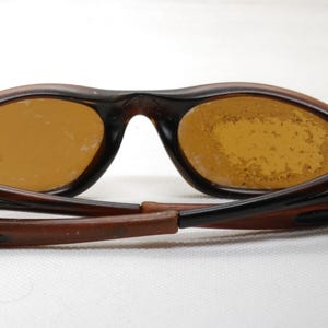 Puede incluir: Gafas de sol marrones con lentes &aacute;mbar. Las monturas son de color marr&oacute;n oscuro y las patillas est&aacute;n plegadas. Las lentes presentan algunas imperfecciones. Las gafas de sol est&aacute;n dise&ntilde;adas para proteger los ojos de la luz solar.