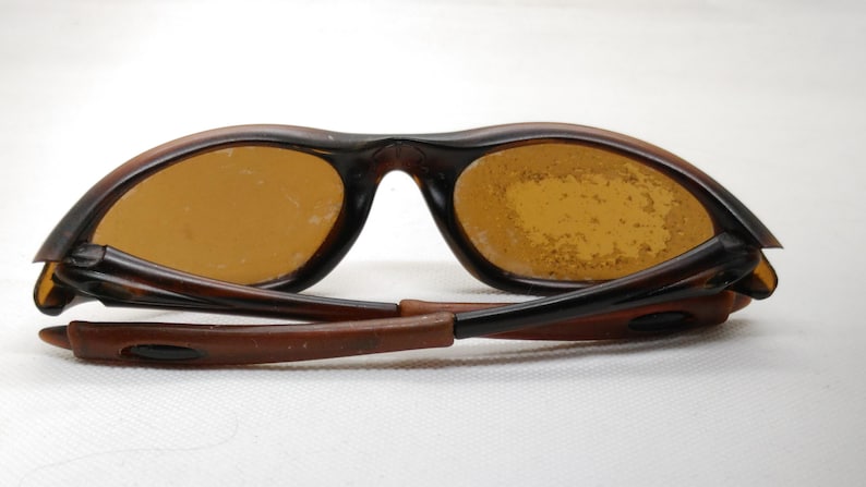 Puede incluir: Gafas de sol marrones con lentes &aacute;mbar. Las monturas son de color marr&oacute;n oscuro y las patillas est&aacute;n plegadas. Las lentes presentan algunas imperfecciones. Las gafas de sol est&aacute;n dise&ntilde;adas para proteger los ojos de la luz solar.
