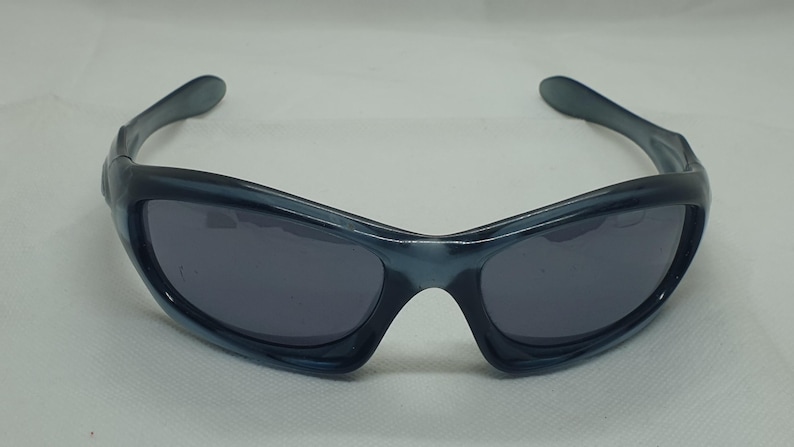 May include: Sport sunglasses with a wraparound design. The frames are a translucent blue-gray, and the lenses are a dark gray. The sunglasses have a sleek, modern aesthetic, suitable for outdoor activities and sports.