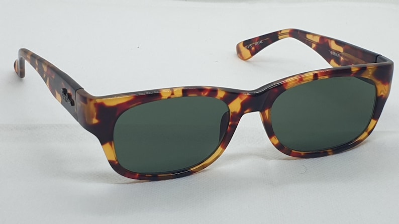 Puede incluir: Gafas de sol carey con lentes verde oscuro. Las monturas tienen un patr&oacute;n cl&aacute;sico marr&oacute;n y amarillo. Las patillas se curvan ligeramente y las lentes son ovaladas. Un peque&ntilde;o logotipo es visible.
