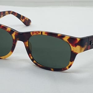 Puede incluir: Gafas de sol carey con lentes verde oscuro. Las monturas tienen una forma rectangular cl&aacute;sica con un patr&oacute;n moteado marr&oacute;n y amarillo. Las patillas presentan un peque&ntilde;o logotipo. Un accesorio elegante para la protecci&oacute;n ocular.