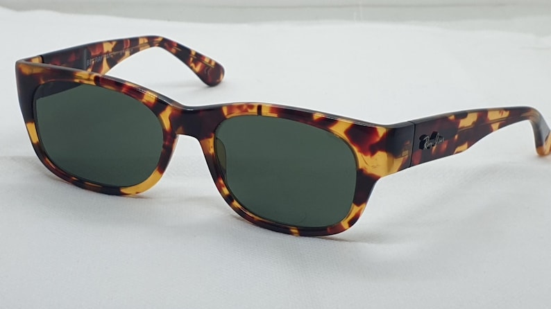 Puede incluir: Gafas de sol carey con lentes verde oscuro. Las monturas tienen una forma rectangular cl&aacute;sica con un patr&oacute;n moteado marr&oacute;n y amarillo. Las patillas presentan un peque&ntilde;o logotipo. Un accesorio elegante para la protecci&oacute;n ocular.