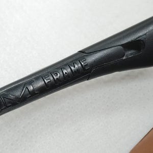 May include: A close-up shot of a black M Frame eyewear arm. The words "M FRAME" are embossed on the arm. The arm is made of a matte black material and has a sleek, modern design.