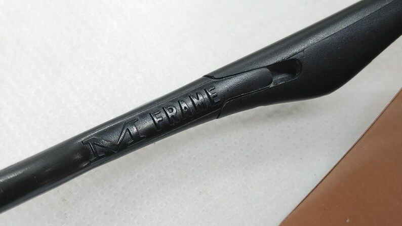 May include: A close-up shot of a black M Frame eyewear arm. The words "M FRAME" are embossed on the arm. The arm is made of a matte black material and has a sleek, modern design.