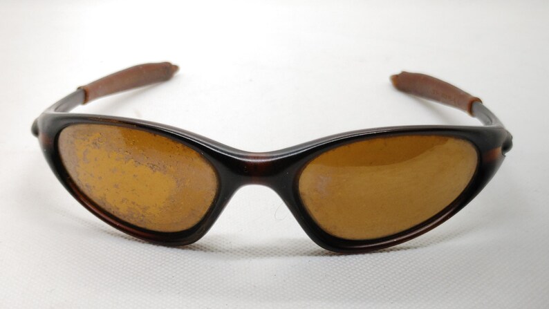 Puede incluir: Gafas de sol marrones con montura curvada y lentes color &aacute;mbar. Las patillas son de un color marr&oacute;n m&aacute;s oscuro. Las gafas de sol est&aacute;n dise&ntilde;adas para proteger los ojos del sol.