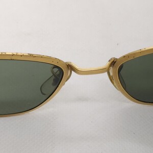 May include: Vintage sunglasses with a gold metal frame and dark green lenses. The arms feature a tortoiseshell pattern. The glasses have a classic, retro design.