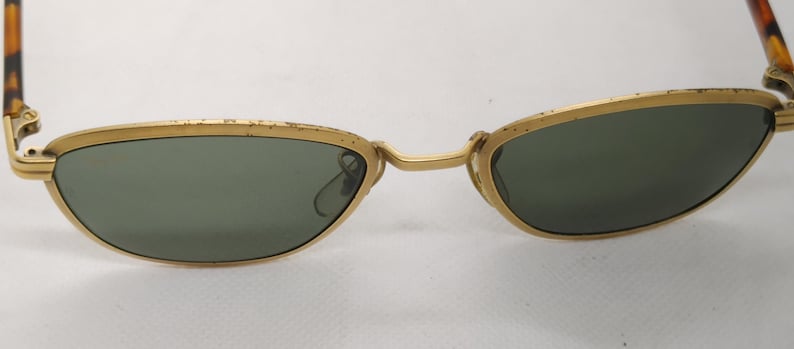 May include: Vintage sunglasses with a gold metal frame and dark green lenses. The arms feature a tortoiseshell pattern. The glasses have a classic, retro design.