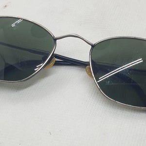 Puede incluir: Gafas de sol vintage con montura de metal plateado y lentes verde oscuro. Las lentes ovaladas est&aacute;n en una montura fina con varillas negras. Un accesorio de gafas cl&aacute;sico.
