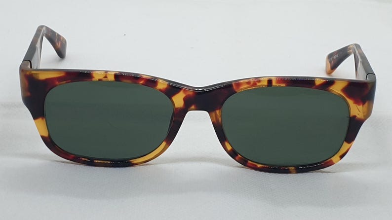 Puede incluir: Gafas de sol con montura cl&aacute;sica de carey y lentes verde oscuro. Las gafas de sol tienen forma rectangular con bordes redondeados. La montura presenta una mezcla de tonos marrones, negros y amarillos.