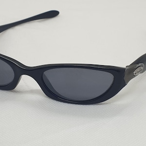 May include: Black sunglasses with a sleek, curved design. The lenses are a dark grey, and the frames are a glossy black. The temples curve gracefully, and the arms are thin. A small, metallic accent is visible on the side of the frame.