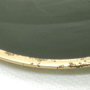 May include: Close-up of vintage sunglasses with a gold-colored metal frame and dark green lenses. The frame shows signs of wear and age, with some discoloration and spots. The lenses are slightly curved and reflect the light.