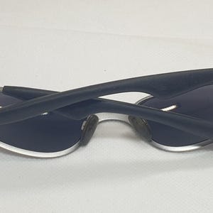 K&ouml;nnte beinhalten: Sonnenbrille mit silbernem Rahmen und dunkelblauen Gl&auml;sern. Die B&uuml;gel sind schwarz und gebogen. Die Sonnenbrille ist zusammengeklappt und zeigt die Innenseite der Gl&auml;ser.