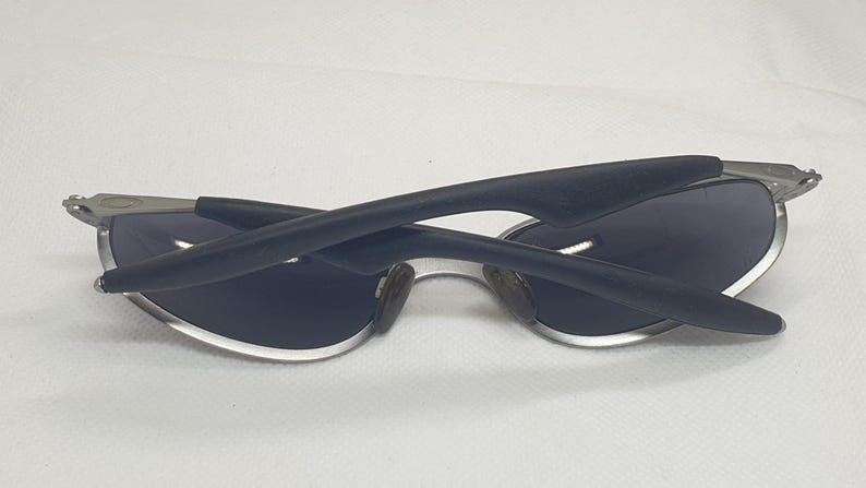 K&ouml;nnte beinhalten: Sonnenbrille mit silbernem Rahmen und dunkelblauen Gl&auml;sern. Die B&uuml;gel sind schwarz und gebogen. Die Sonnenbrille ist zusammengeklappt und zeigt die Innenseite der Gl&auml;ser.