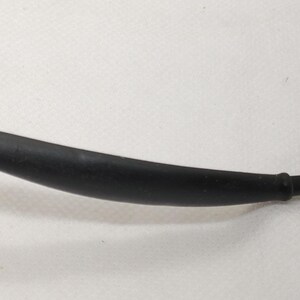 May include: A curved, black rubber component with a cylindrical end. The object appears to be a part of a larger mechanism or device, possibly a hose or a handle. The surface is smooth and matte.