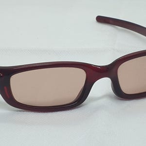 May include: Burgundy sunglasses with rectangular lenses. The frames are a deep red colour, and the lenses have a light brown tint. The sunglasses have a sleek, modern design, suitable for outdoor activities.
