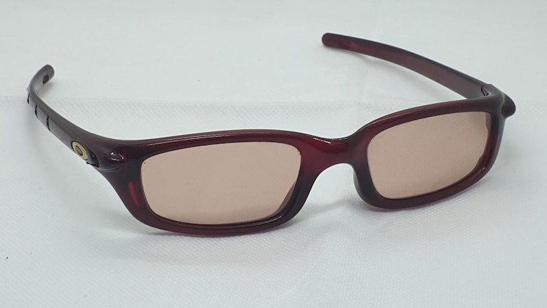May include: Burgundy sunglasses with rectangular lenses. The frames are a deep red colour, and the lenses have a light brown tint. The sunglasses have a sleek, modern design, suitable for outdoor activities.
