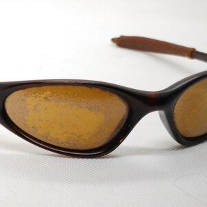 Puede incluir: Gafas de sol marrones con lentes &aacute;mbar. Las monturas son de color marr&oacute;n oscuro, con un dise&ntilde;o curvo. Las patillas son de color marr&oacute;n claro. Las lentes muestran signos de desgaste.