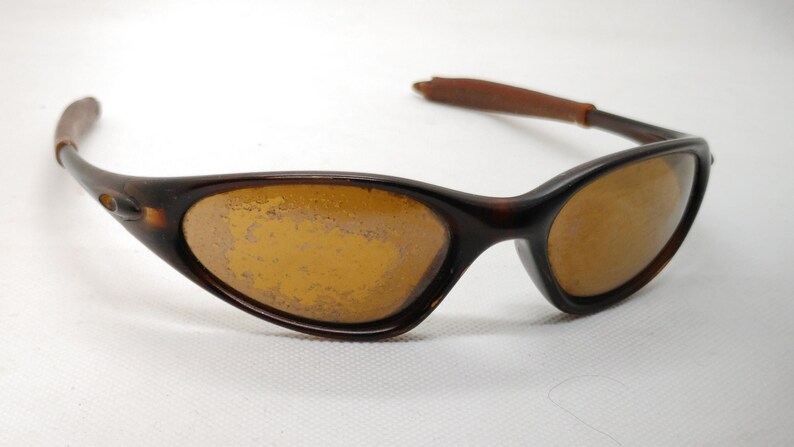 Puede incluir: Gafas de sol marrones con lentes &aacute;mbar. Las monturas son de color marr&oacute;n oscuro, con un dise&ntilde;o curvo. Las patillas son de color marr&oacute;n claro. Las lentes muestran signos de desgaste.