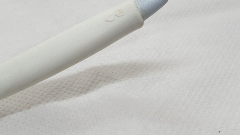 K&ouml;nnte beinhalten: Nahaufnahme eines wei&szlig;en Kosmetikstifts mit hellblauer Spitze. Der Stift hat eine glatte, matte Oberfl&auml;che und liegt auf einer wei&szlig;en, strukturierten Oberfl&auml;che. Die Buchstaben "CE" sind auf den Stift gedruckt.