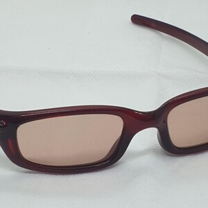 May include: Burgundy sunglasses with a rectangular frame and tinted lenses. The temples are a darker shade of burgundy. The glasses are designed for eye protection from sunlight.