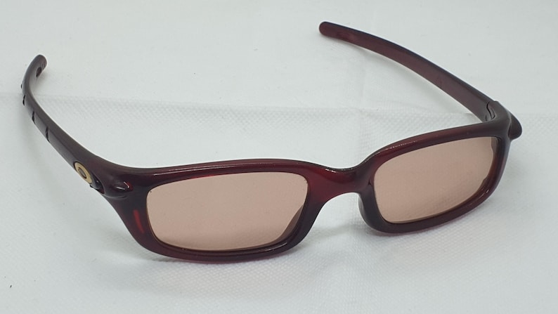 May include: Burgundy sunglasses with a rectangular frame and tinted lenses. The temples are a darker shade of burgundy. The glasses are designed for eye protection from sunlight.