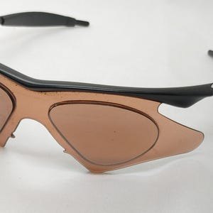 May include: Black and brown sports sunglasses with a curved frame and tinted lenses. The sunglasses have a sleek, modern design, suitable for outdoor activities. The lenses are a light brown colour.