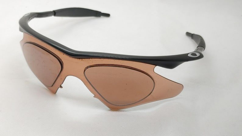May include: Black and brown sports sunglasses with a curved frame and tinted lenses. The sunglasses have a sleek, modern design, suitable for outdoor activities. The lenses are a light brown colour.