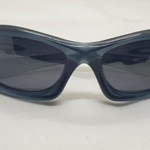 May include: Dark blue sunglasses with a curved, wraparound design. The lenses are a dark gray, and the frames have a glossy finish. These sunglasses are suitable for outdoor activities and offer eye protection.