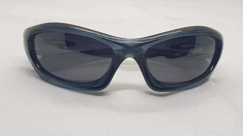 May include: Dark blue sunglasses with a curved, wraparound design. The lenses are a dark gray, and the frames have a glossy finish. These sunglasses are suitable for outdoor activities and offer eye protection.