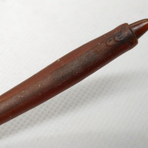 Puede incluir: Una varita de madera marr&oacute;n con una punta. La varita tiene un acabado liso y pulido y parece estar hecha de una sola pieza de madera. La punta es de un tono marr&oacute;n m&aacute;s oscuro.