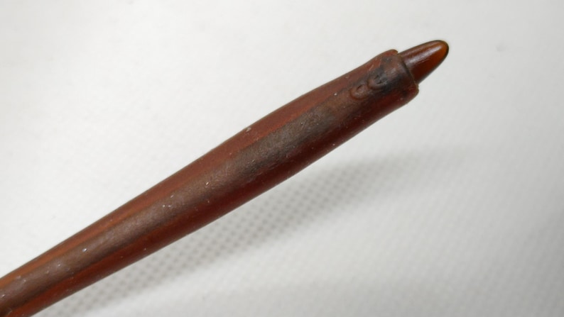 Puede incluir: Una varita de madera marr&oacute;n con una punta. La varita tiene un acabado liso y pulido y parece estar hecha de una sola pieza de madera. La punta es de un tono marr&oacute;n m&aacute;s oscuro.