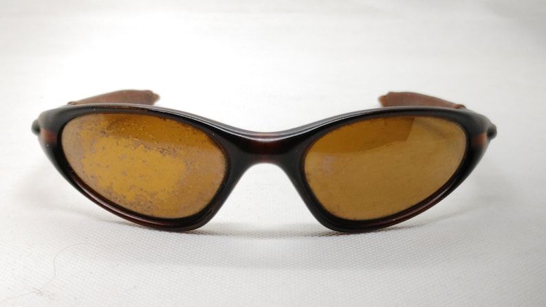 Puede incluir: Gafas de sol marrones con lentes &aacute;mbar. Las gafas tienen una montura marr&oacute;n oscuro y un dise&ntilde;o curvado. Las lentes parecen estar ligeramente rayadas. Las patillas de las gafas son de color marr&oacute;n claro.