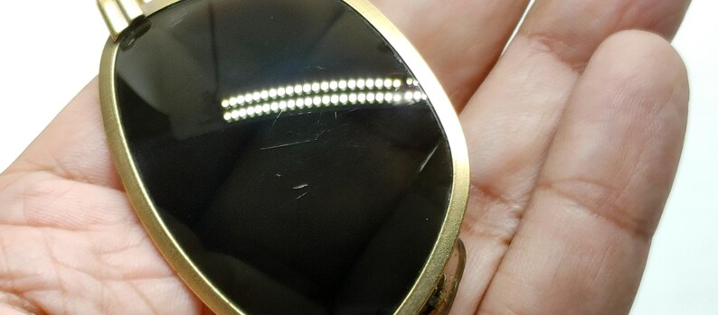 May include: Sunglasses with a gold-colored frame and dark lenses. The sunglasses have a teardrop shape and are held in a hand. The lenses have some scratches.