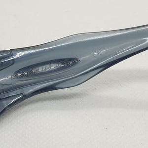 May include: Close-up of a pair of gray sunglasses. The sunglasses have a sleek, modern design with a curved frame. The text "MADE IN USA" is visible on the arm of the sunglasses.