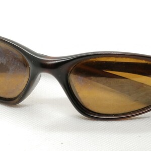 Puede incluir: Gafas de sol marrones con estampado de carey. Las lentes son de color &aacute;mbar c&aacute;lido y las monturas tienen un dise&ntilde;o elegante y curvado. Sobre un fondo blanco.