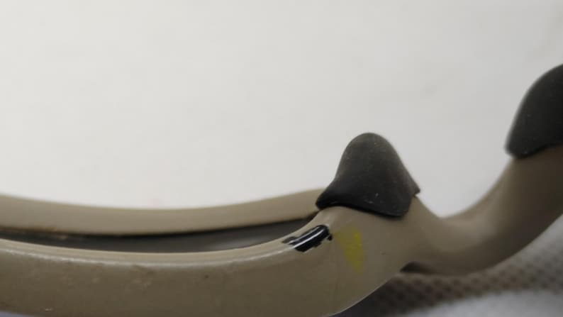 Puede incluir: Primer plano de un objeto de color beige con dos protuberancias redondeadas de color gris oscuro. El objeto tiene una forma curva y parece estar hecho de un material liso. Hay peque&ntilde;as marcas negras y amarillas en la superficie.