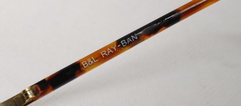 May include: Close-up of a Ray-Ban eyeglass arm with a tortoiseshell pattern. The text "B&L RAY-BAN" is printed in white on the arm. The arm is a mix of brown, black, and amber colors.