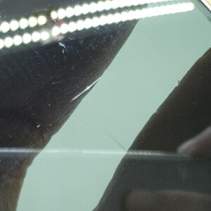 May include: Close-up of sunglasses with a gold-colored frame and green-tinted lenses. The lenses have a slight scratch. The sunglasses are held by a person's fingers.