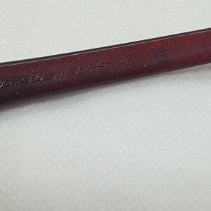 May include: Close-up of a section of eyeglasses. The frame is a dark burgundy colour. The text "MADE IN USA" is visible on the frame.