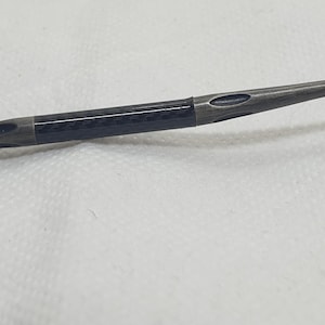 May include: Close-up of a dark gray eyeglass arm with a carbon fiber section. The arm has a sleek, modern design with oval cutouts and a metallic finish. The hinge is visible on the left side.