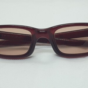 May include: Burgundy sunglasses with rectangular frames and tinted lenses. The glasses have a classic design. The arms of the glasses are folded. Suitable for everyday wear.